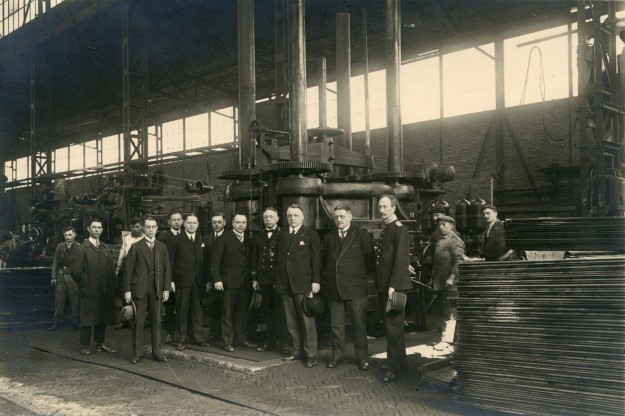 Bedrijfsbezoek van het Ministerie van Defensie met directeur J.P. van Heijst, poserend voor een grote pers. J.B. van Heijst, metaalconstructies, Cruquiuskade, ca. 1915