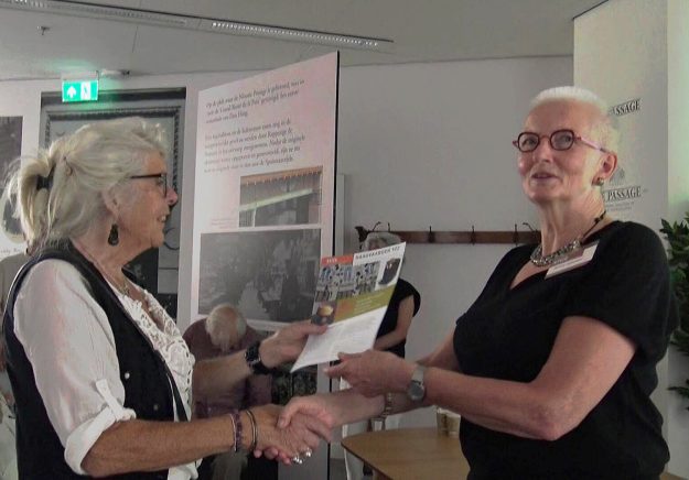 Jannie Havelaar overhandigt het eerste exemplaar van Haagvaarder 122 aan Thea van der Helm, voormalig eigenaar Ladies Paradise, 2024. SHIE presentatie , Passage, 2024