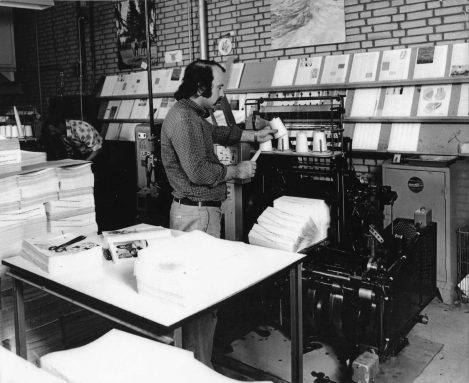 De heer Uljee bij één van de bindmachines met aan de wand het uitgelegde voorbeeld van het te binden boek. Van Rijmenam, Fruitweg 17, jaren 70