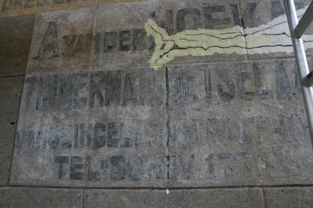 Een reparatie van een scheur. Gaten worden afgetaped met schilderstape zodat het plamuur niet verder op de muur komt. Na het uitharden wordt de tape verwijderd. Op basis van onderzoek in de oude telefoongidsen kan deze muurreclame gedateerd worden op 1911-1912. Muurreclame, Van der Hoek, Frederik Hendriklaan, 2014